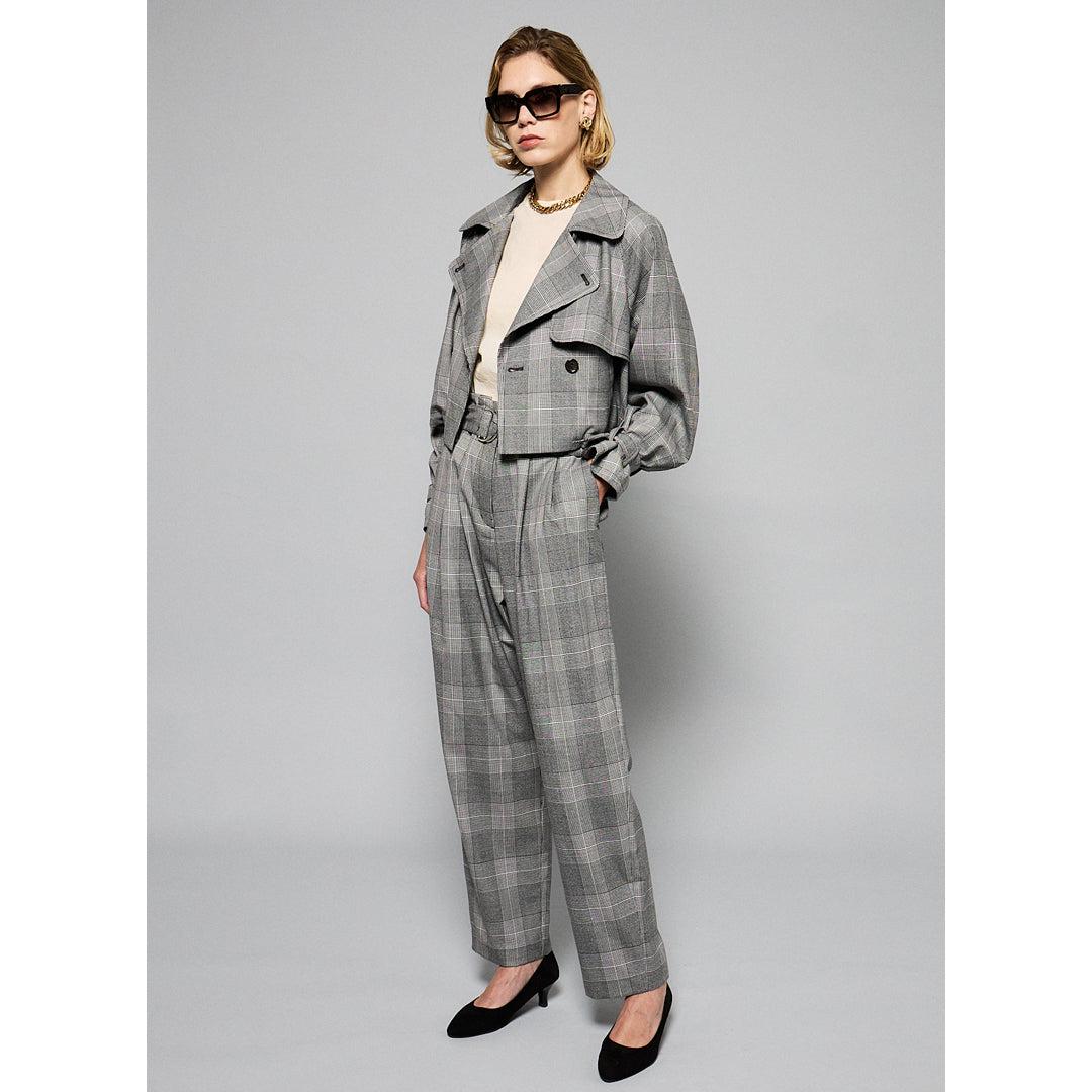 A person with short, blonde hair wearing large, dark sunglasses, a light chain necklace, and a chic Marie Cropped Glen Plaid Jacket by Maison Lilli over a light-colored shirt. The flattering silhouette exudes a stylish and modern vibe against a plain gray background.